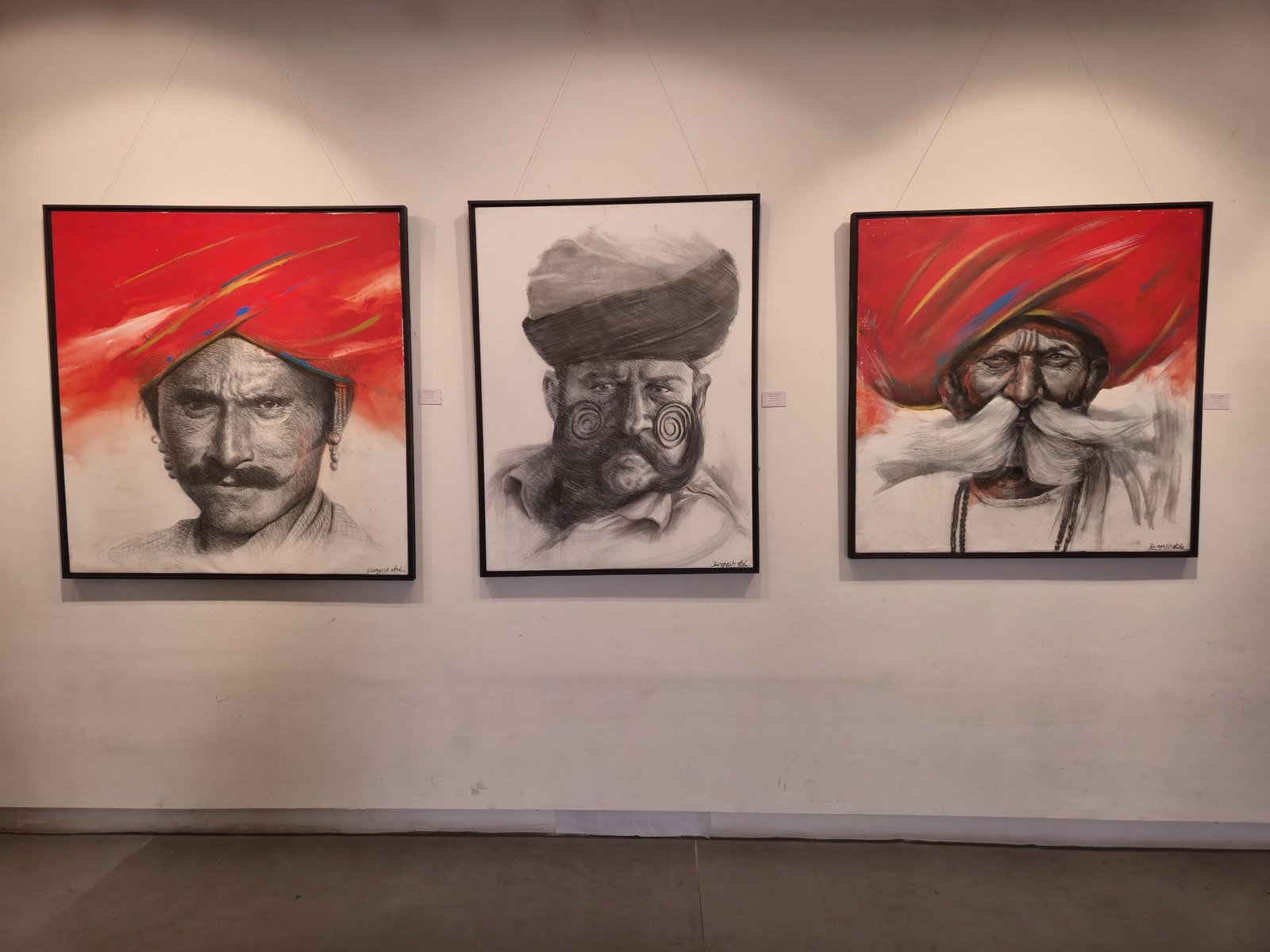 Three framed charcoal and acrylic portraits on a gallery wall